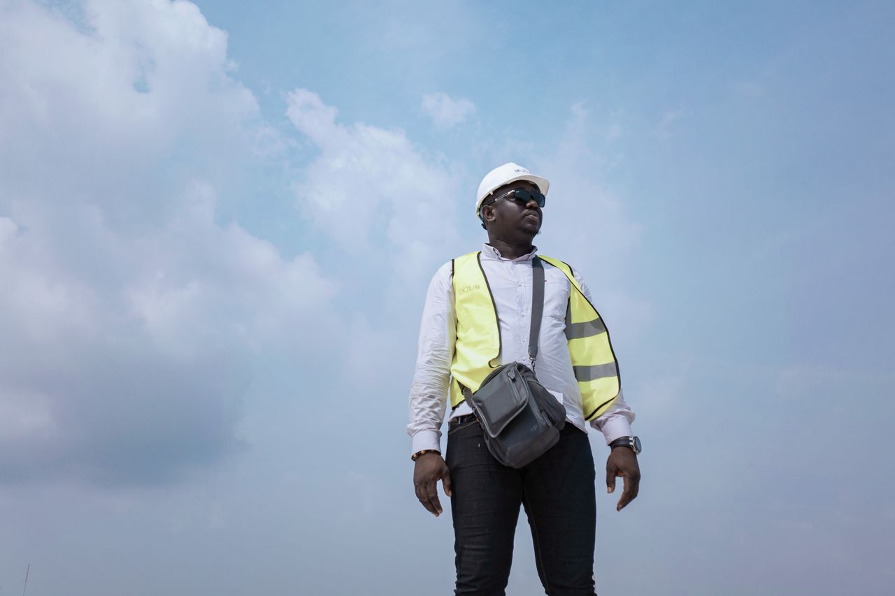 A man wearing a reflective vest and hard hat looks confident against a clear sky.