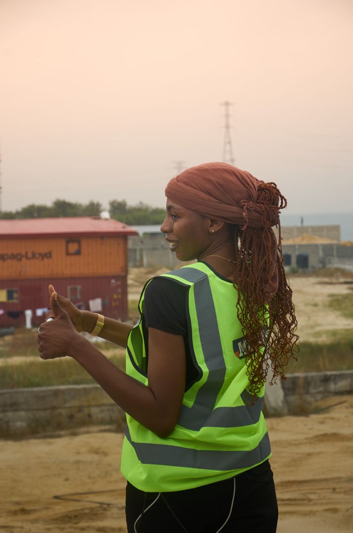 Confident female construction worker in safety vest giving thumbs up at a building site.