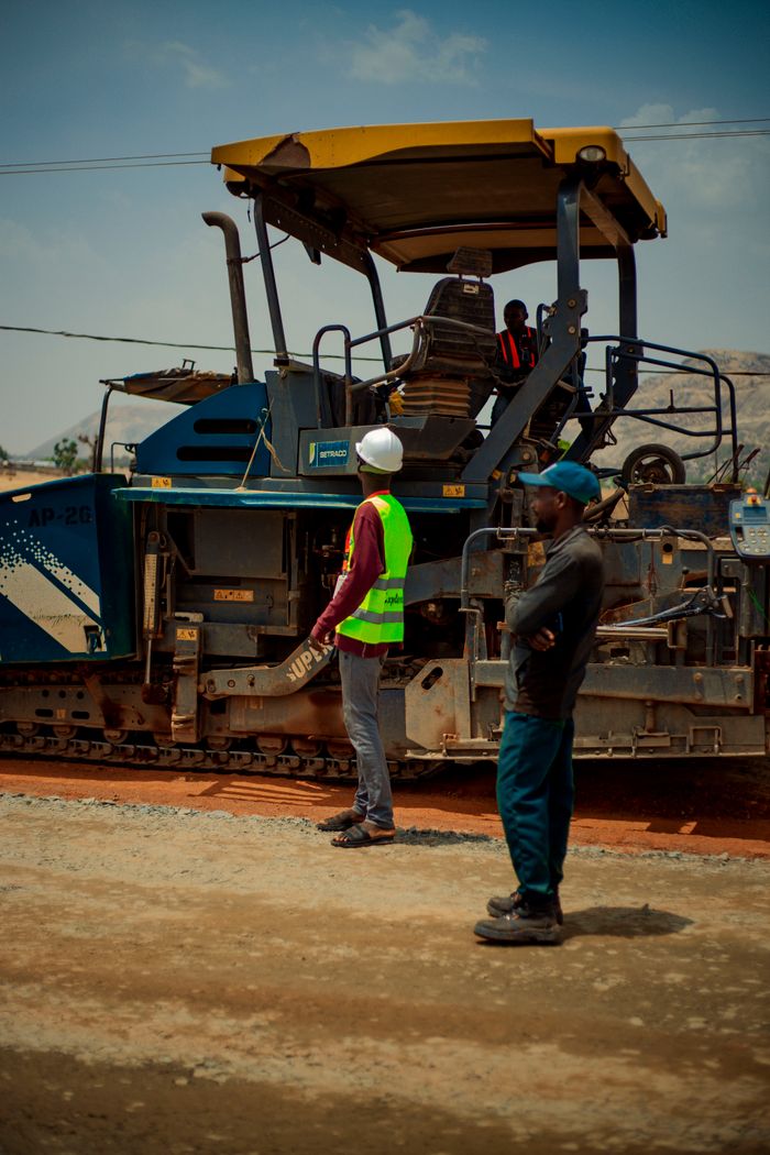 Two construction workers observing roadwork machinery under bright daylight.