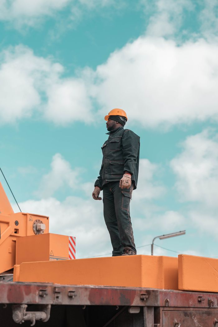 A construction worker stands on a crane against a blue sky, symbolizing strength and industry.